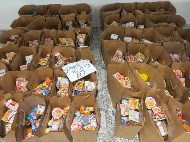Rows of paper grocery bags packed with food, with a handwritten sign counting sixty bags.
