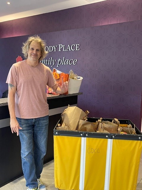Chris standing beside a cart of packed food bags at a family resource center.